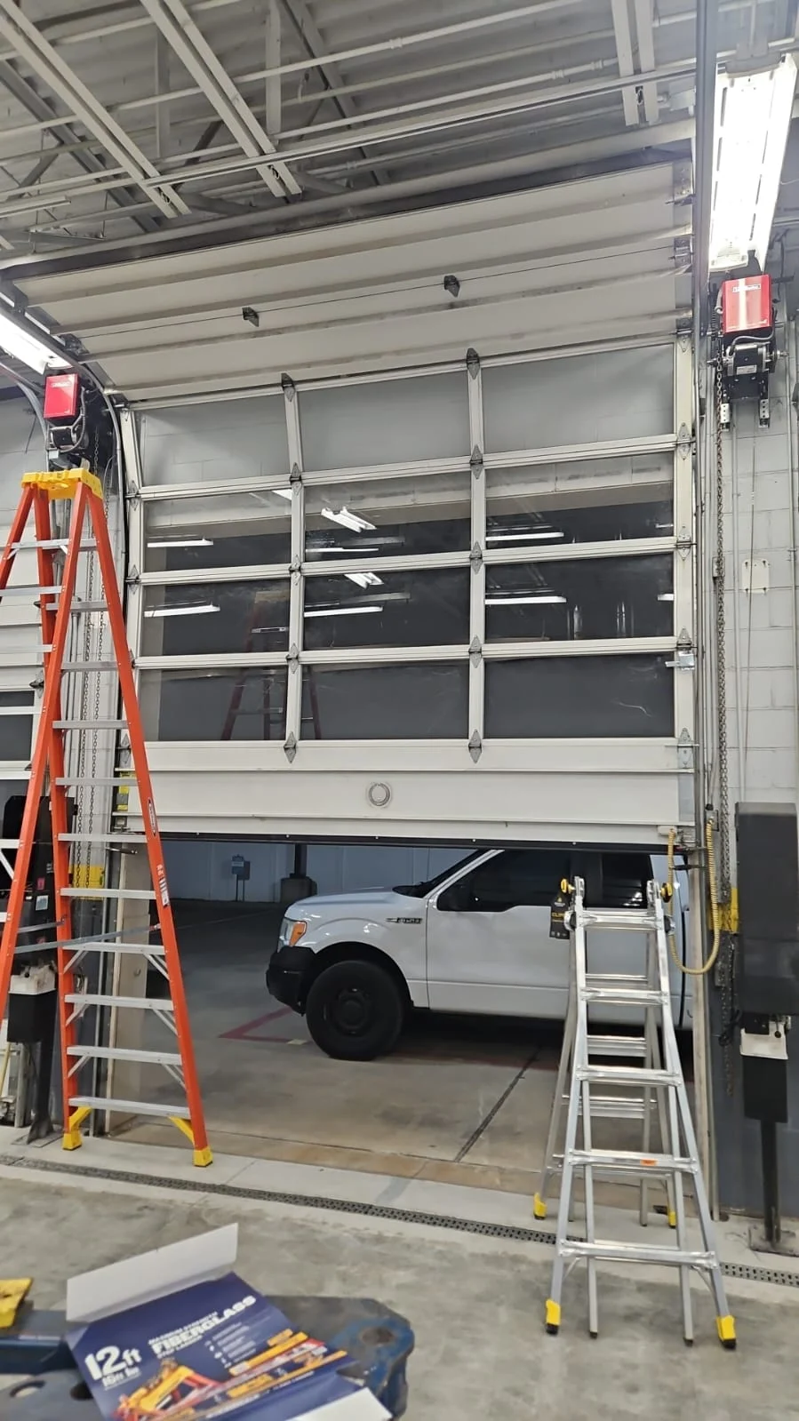 Commercial garage door repair on a full-view sectional overhead door with glass panels inside a commercial service facility.