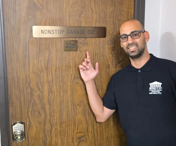Itzhak Levi, the owner pointing at a door labeled "NONSTOP GARAGE DOOR" with the suite number 205