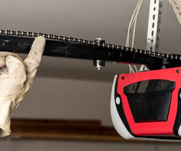 Hand adjusting a garage door opener chain with a red motor unit, illustrating repair and maintenance services for garage door openers in Houston.