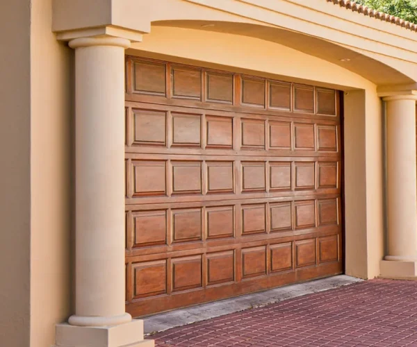 Wooden garage door with decorative panels, framed by architectural columns, representing commercial garage door solutions in Houston.